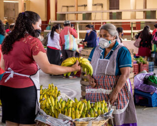 Kvinne med åndedrettsvern kjøper bananer på markedet