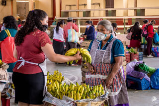 Kvinne med åndedrettsvern kjøper bananer på markedet